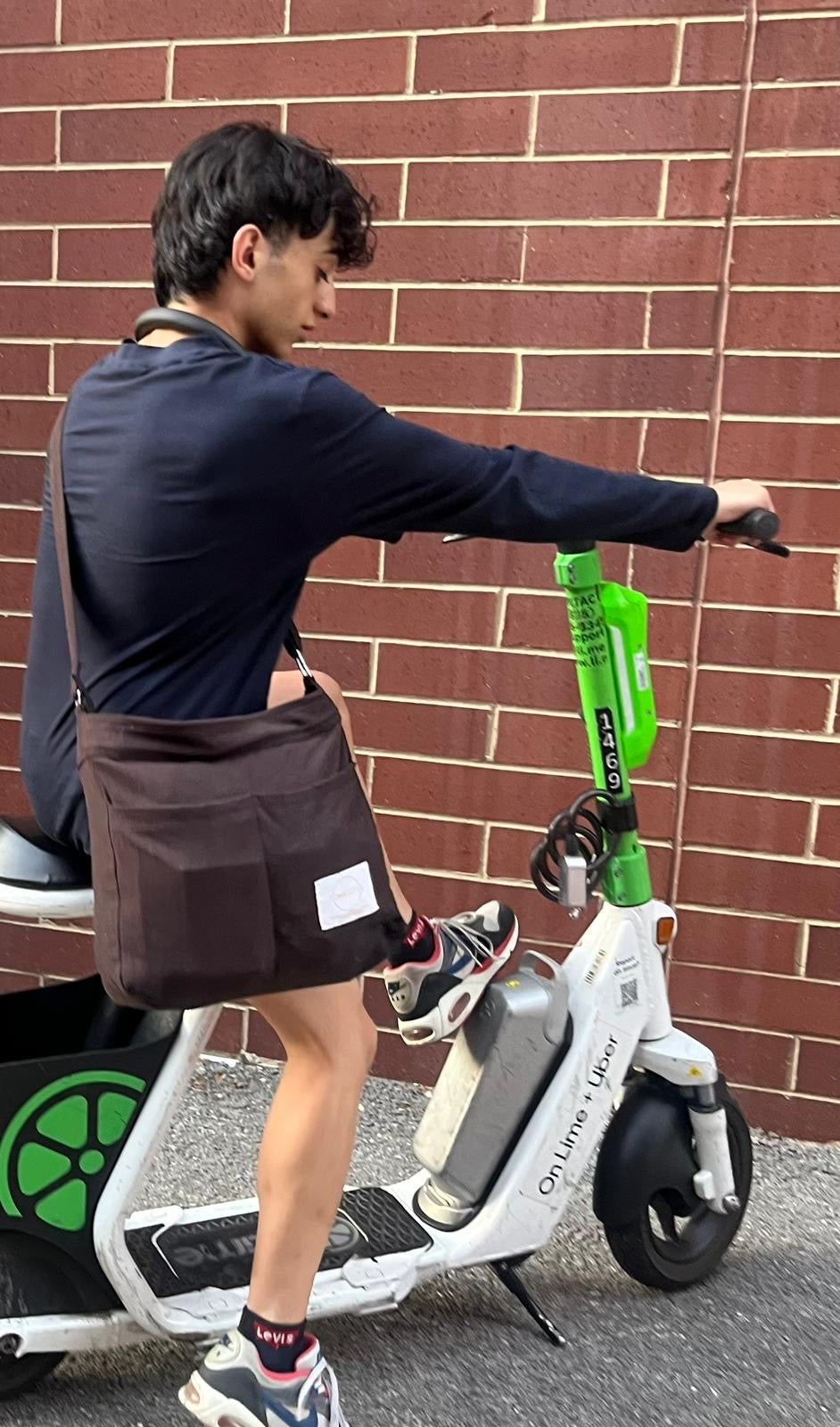 Person using a scooter with a visible brand logo against a brick wall.