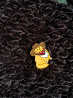 Small yellow bear pin with a cowboy hat on a textured black background