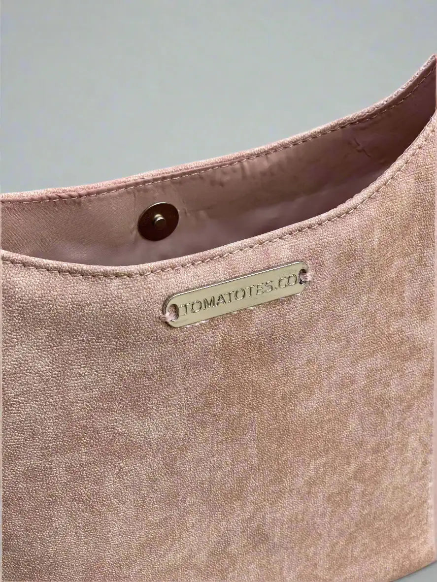 Close-up of a pale pink handbag with a brand label on a neutral background