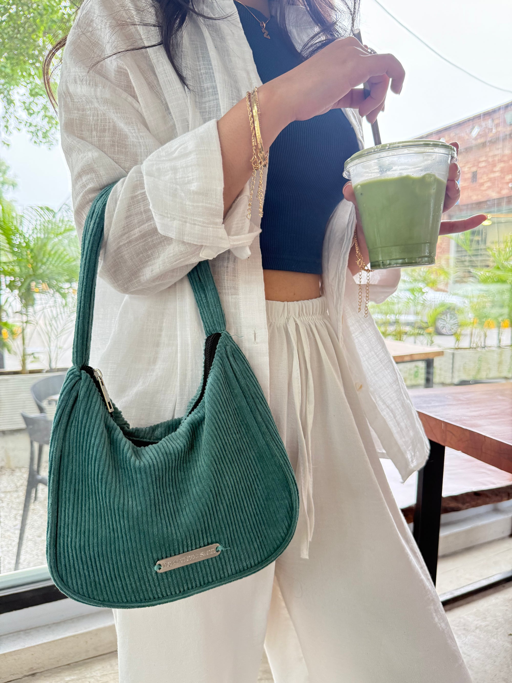 Person holding a green drink and a green handbag in an outdoor setting