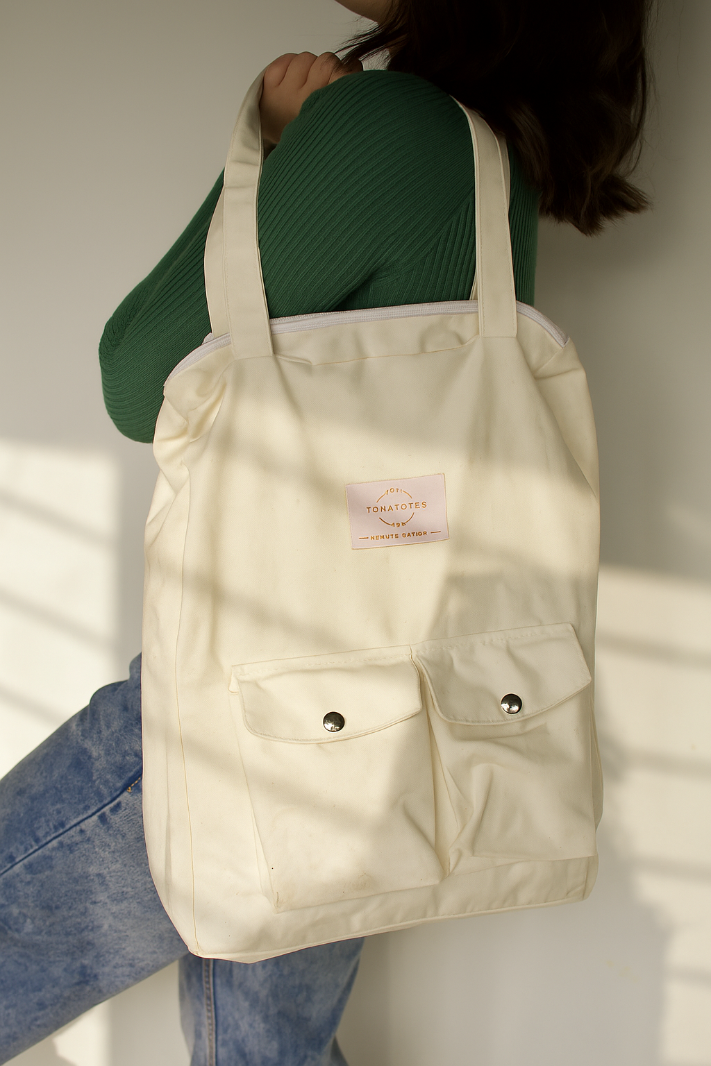 Beige tote bag with a brand label held by a person against a neutral background