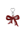A red acrylic bow charm with a silver metal clip on a textured background.