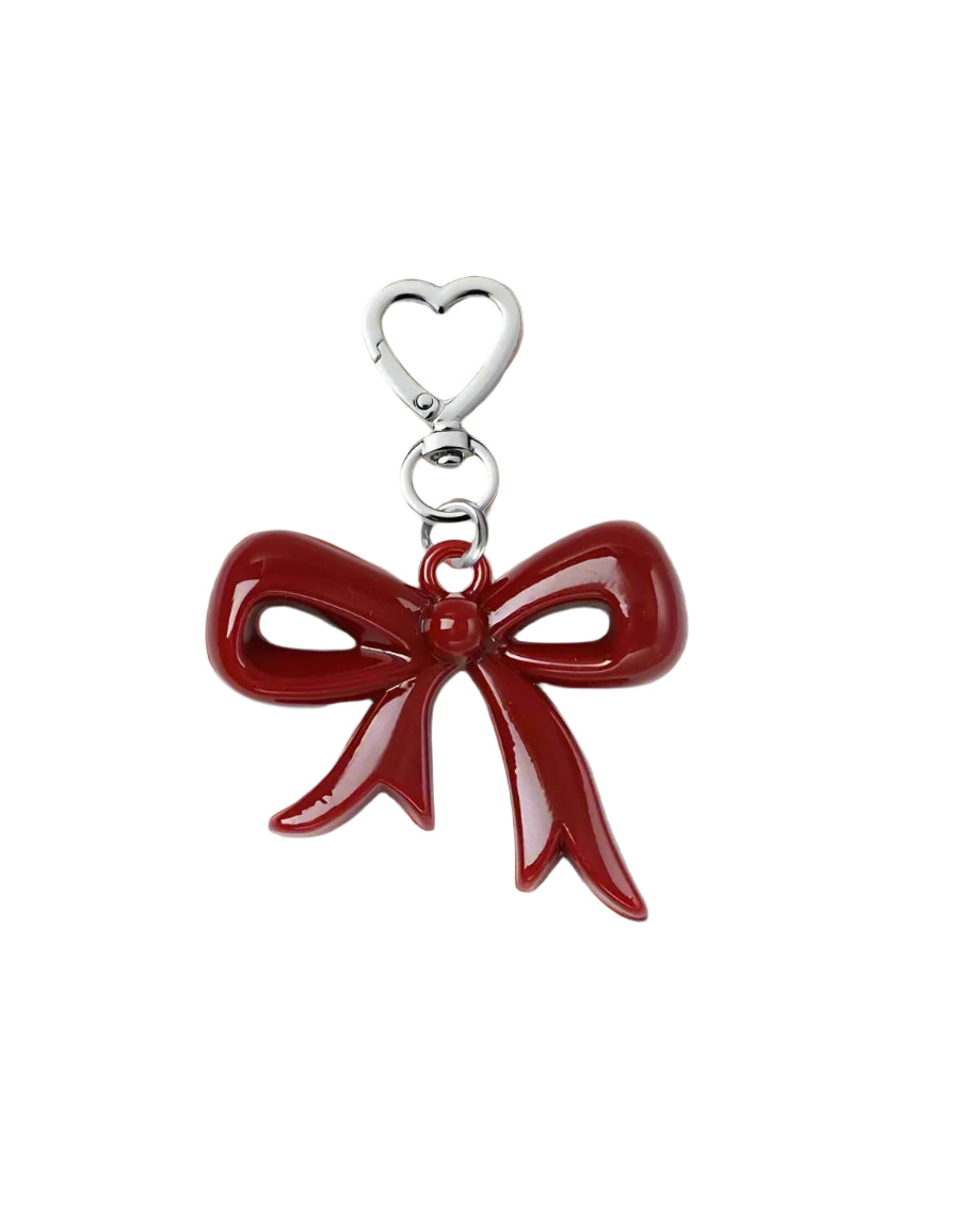 A red acrylic bow charm with a silver metal clip on a textured background.