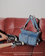 Blue denim bag on a red couch with a person wearing black sneakers.