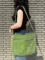 Person holding a green shoulder bag against a brick wall